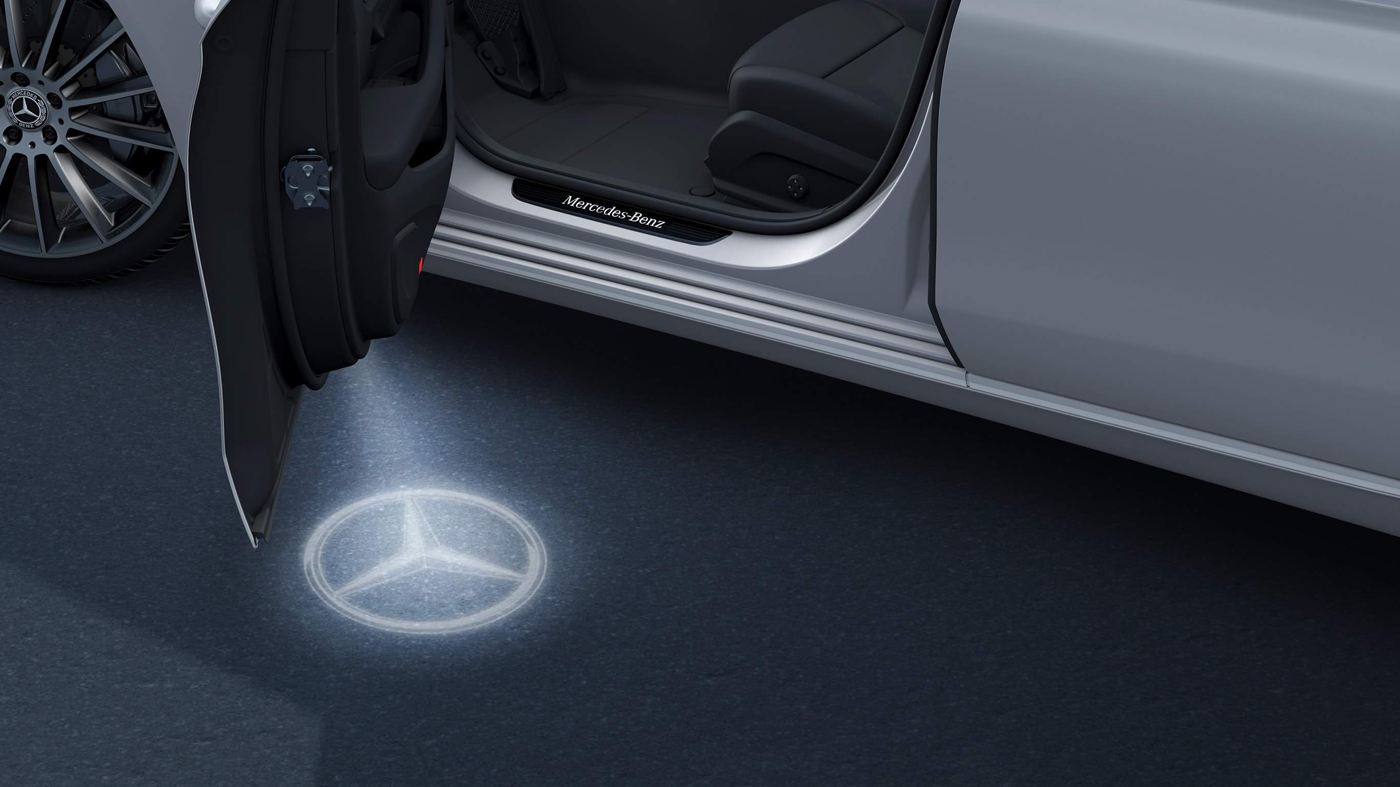 Na obrázku je EQA od Mercedes-EQ s orientačním osvětlením. Orientační osvětlení promítá logo značky v technologii LED vedle otevřených předních dveří.
